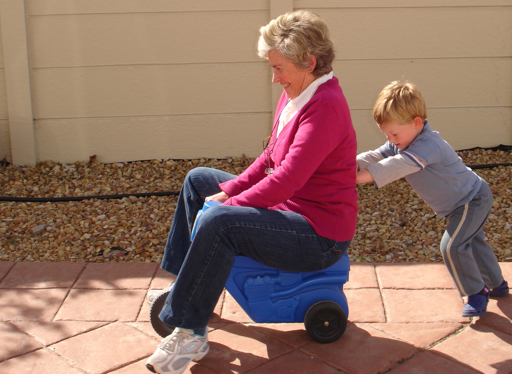 Grandmother riding on a toy tricycle being pushed by her grandson