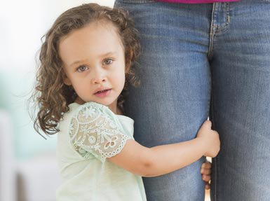 a little girl holding onto her mother's thigh